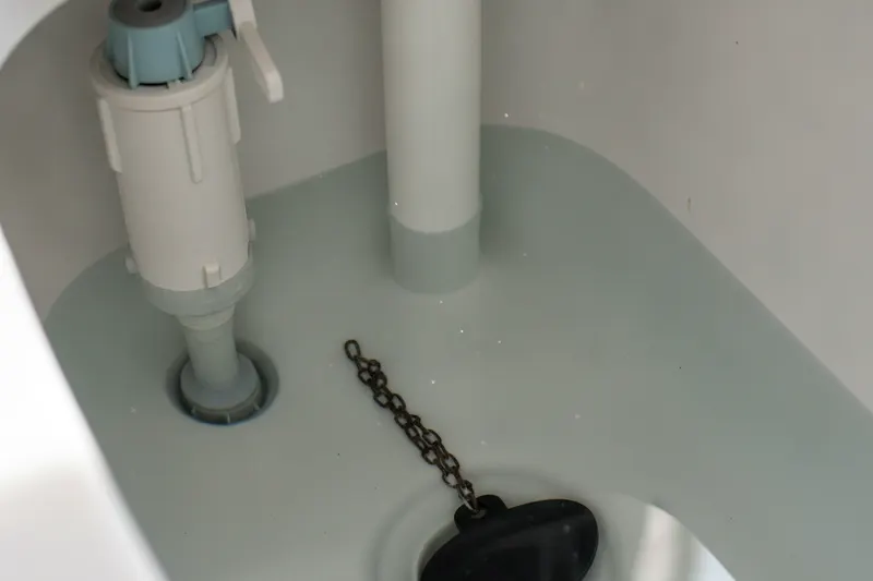 Inside an open toilet tank showing the fill valve, the overflow tube and the rubber flapper with its chain
